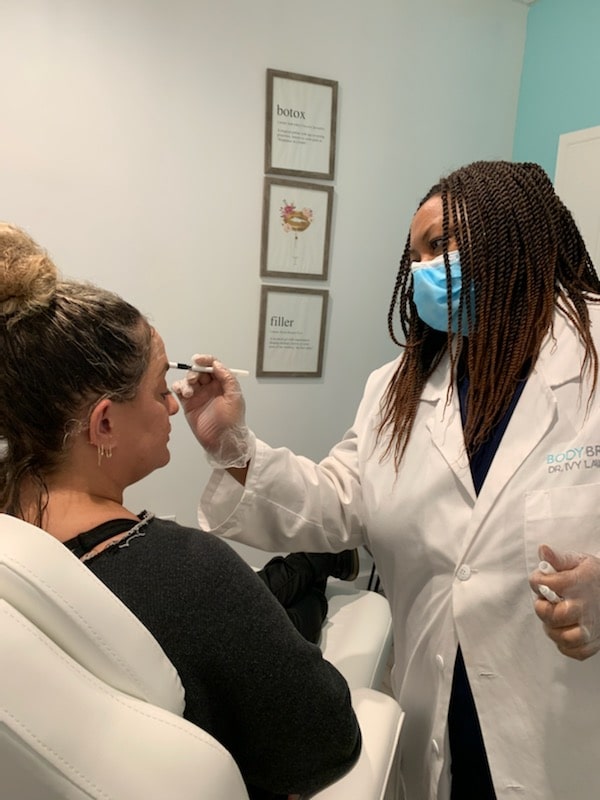 In a Cooper City med spa, a medical professional dressed in a white coat and face mask administers an injection to a seated patient, exemplifying the advanced and personalized care available in this serene setting.