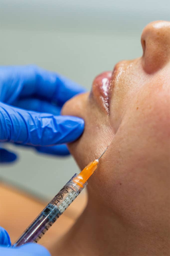 A close-up scene of a person receiving an injection in the cheek from a healthcare professional at a med spa in Cooper City, with the practitioner wearing blue gloves.