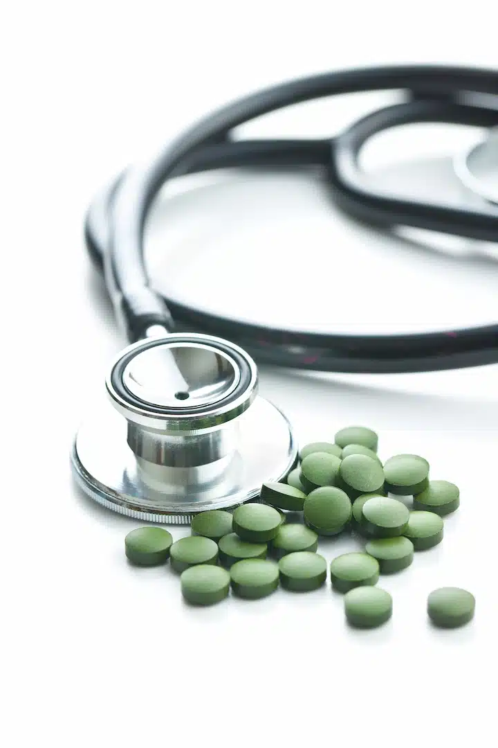 A stethoscope lies next to a pile of green HRT pills on a white surface, reflecting the intersection of traditional medical practices and modern treatments offered at med spas. In places like Cooper City, med spas provide hormone replacement therapy (HRT) alongside other wellness services, blending healthcare and beauty therapies for comprehensive wellbeing solutions.